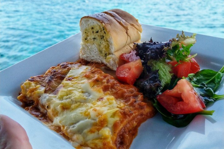 Lasagna and salad on plate with ocean view in background.