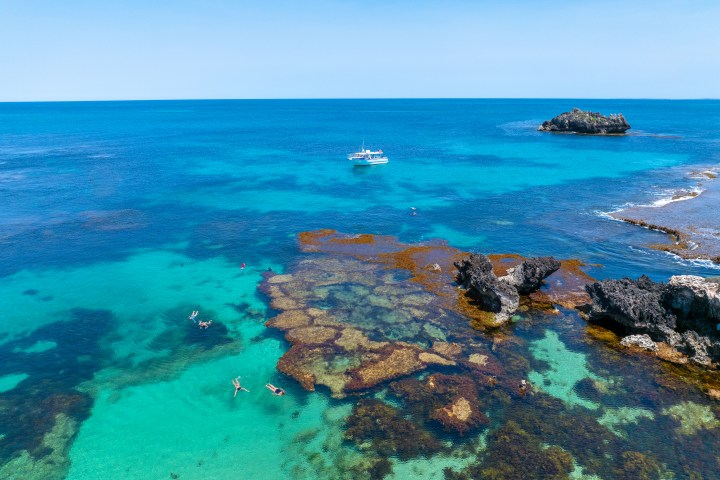 Aerial view of swimmers near coral reef, boat in blue ocean.