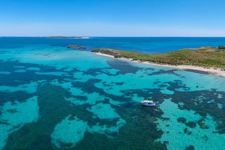 Aerial view of a turquoise sea with a boat near a green island under a clear blue sky.