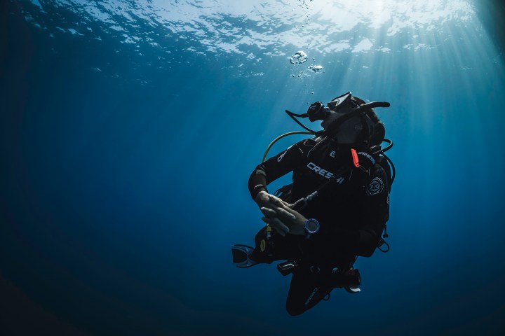 Scuba diver underwater with light rays shining down through the water.