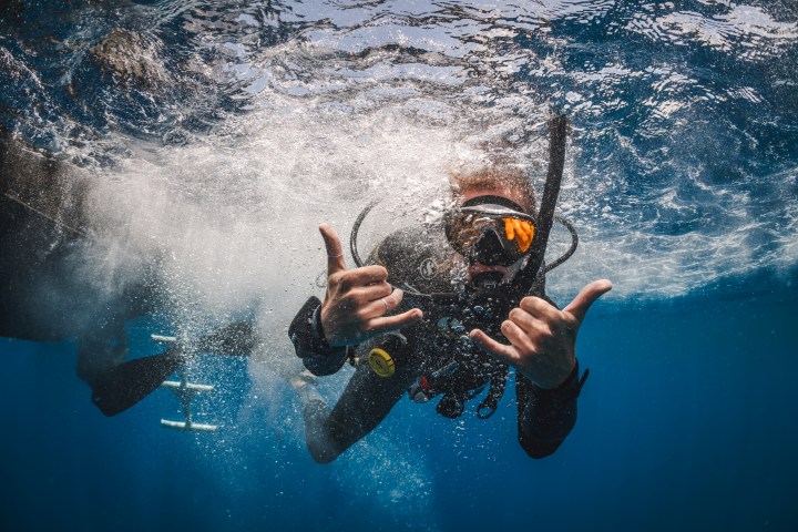 Scuba diver underwater making hand gestures near a ladder.
