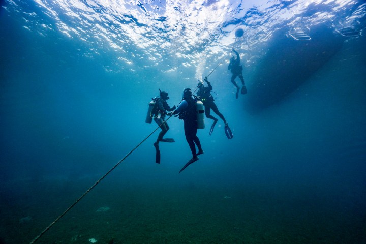 Group of scuba divers underwater, with one diver holding a rope.