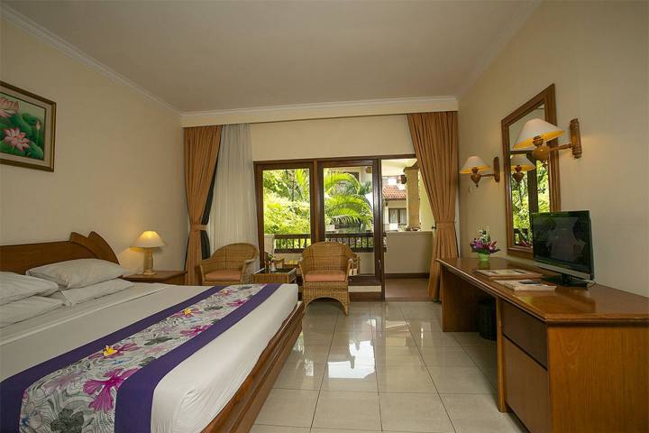 Hotel room with a bed, desk, TV, chairs, and a balcony view.