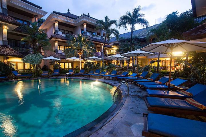 Tropical resort pool with lounge chairs, umbrellas, and palm trees at dusk.