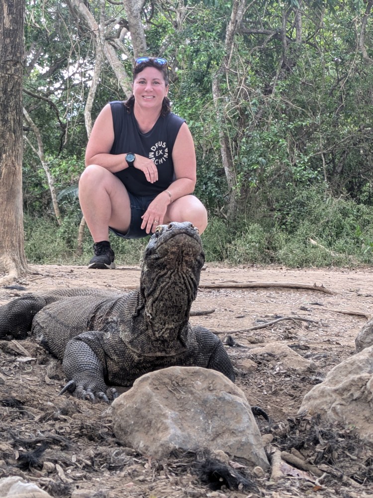 Person posing with a Komodo dragon in a wooded area.