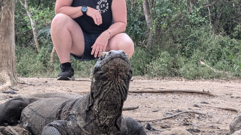 Person posing with a Komodo dragon in a wooded area.
