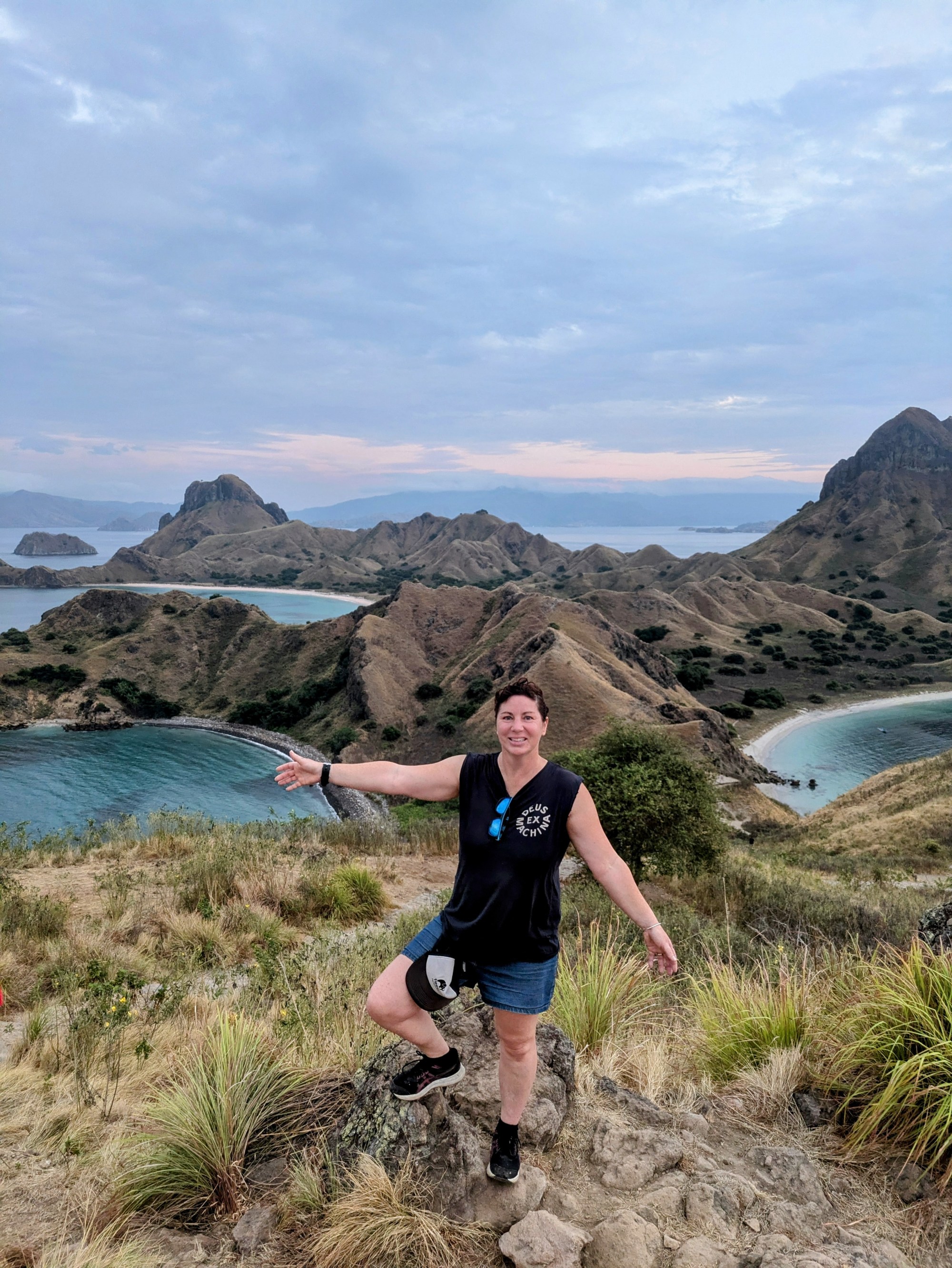 1000002799 (1) Person posing on a hill with arms outstretched, overlooking a coastal landscape.
