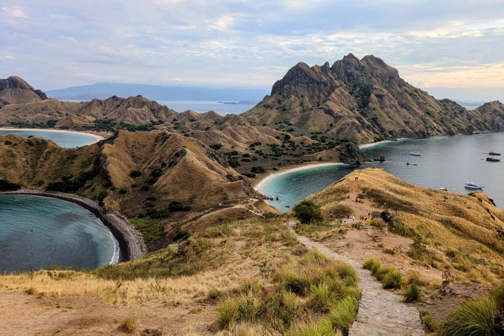 Mountainous island landscape with beaches and boats in the ocean, under a cloudy sky.