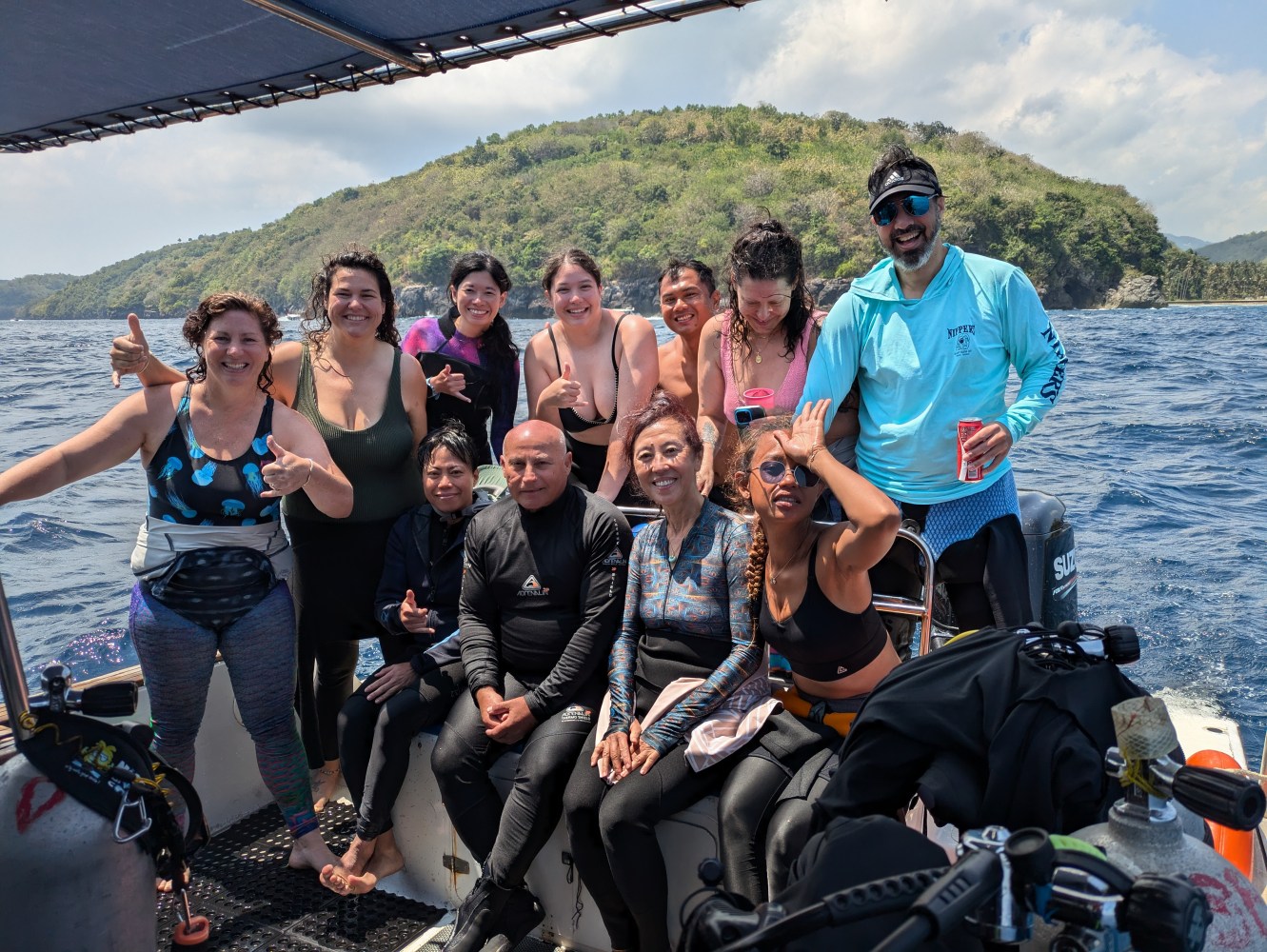 Group of people on a boat in swimwear posing with a scenic island backdrop.