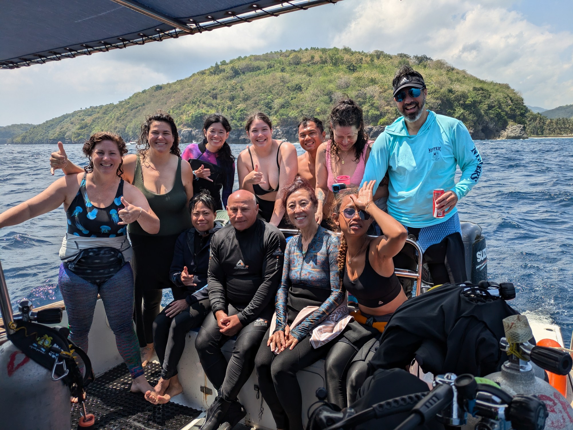 1000004475 Group of people on a boat in swimwear posing with a scenic island backdrop.