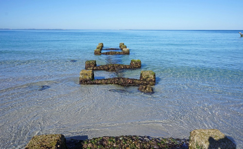 Remains of a pier in calm blue sea with clear sky.