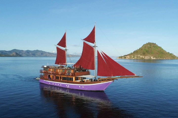 Sailing ship with red sails on calm water near an island.