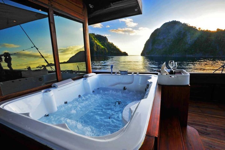 Hot tub on a boat deck with ocean and cliff view during sunset.